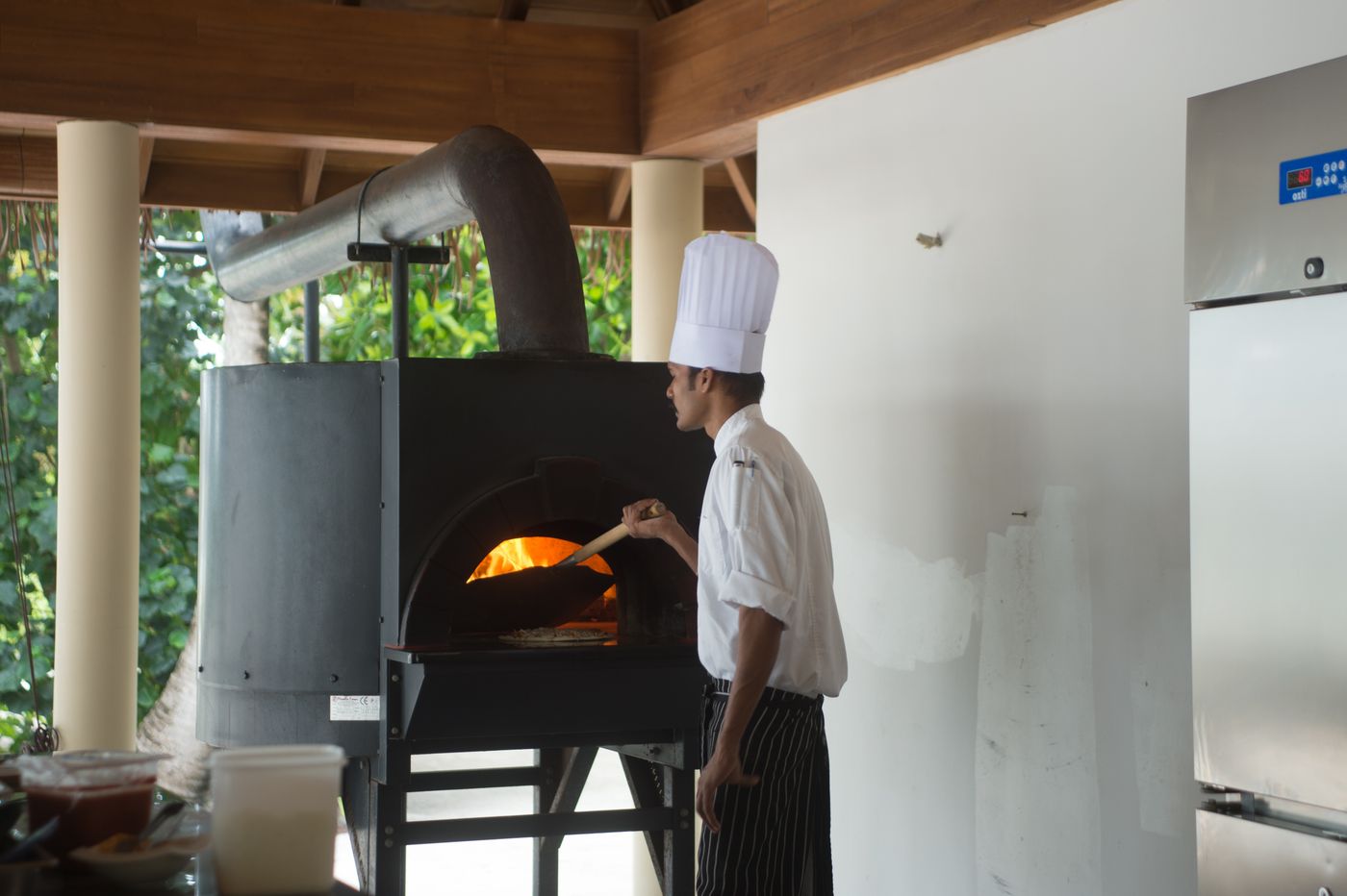 A chef in whites working at a domed wood-fired oven